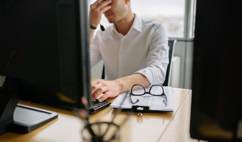 Man sitting at desk in front of computer, with his hands over his eyes in disdain
