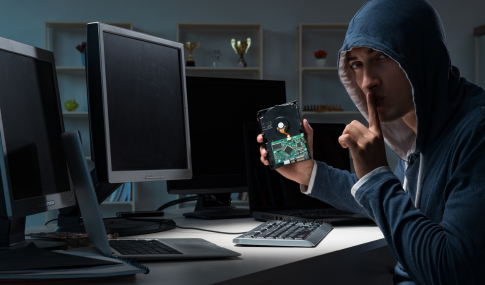 Image with a guy in a hoodie shushing with his finger and pulling out a mother board of a computer