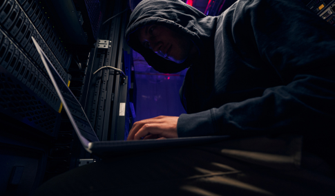 Dark image of a guy in a hoodie while working on a laptop